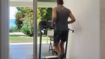Una persona corre en una cinta de correr dentro de una habitación con vistas a un jardín y un cuerpo de agua.