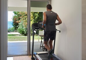 A person running on a treadmill inside a room with a view of a garden and a body of water outside. - Pomos Beachfront Villa (Pomos)