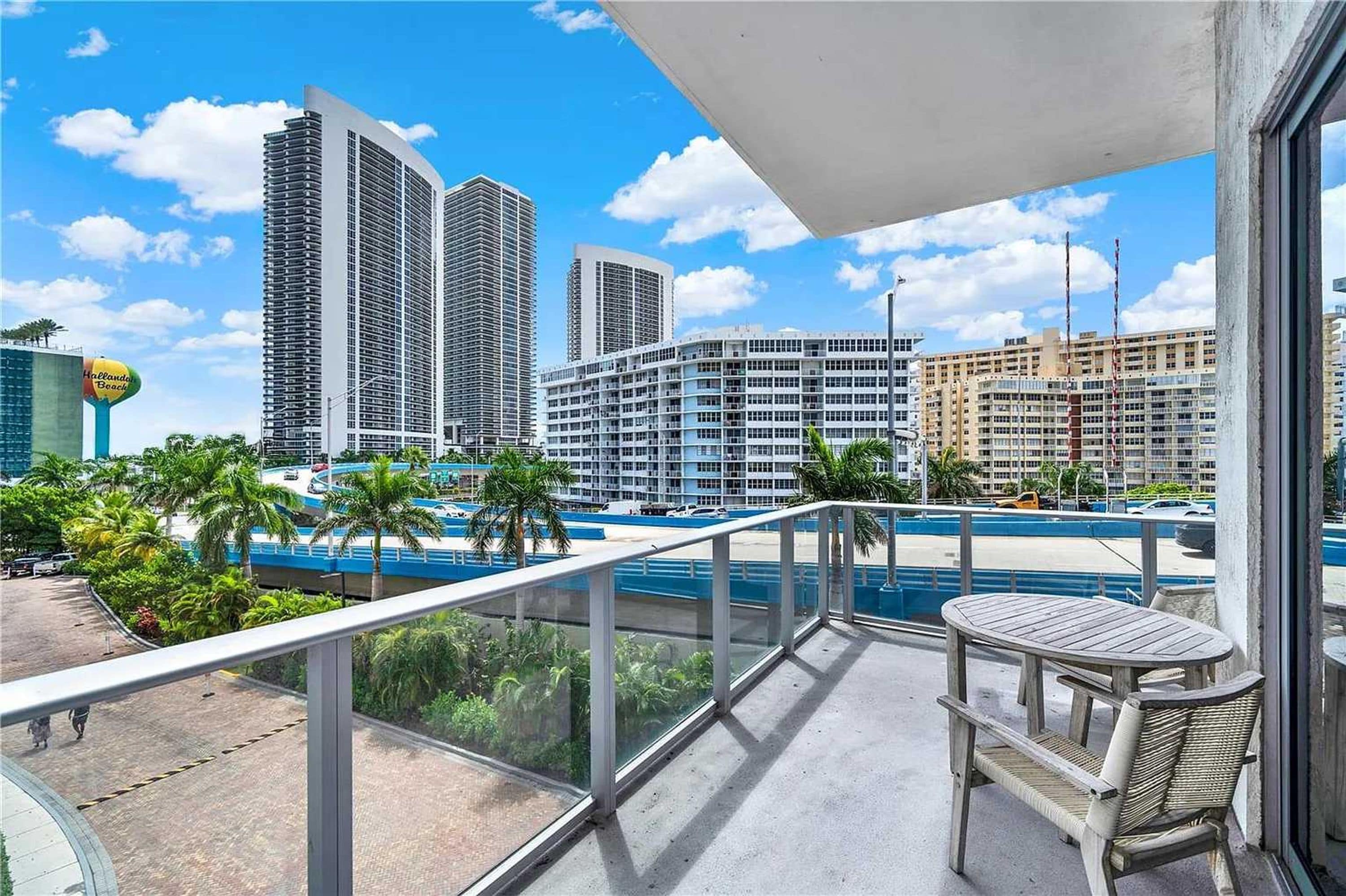 Un balcón con vista a un paisaje urbano, que incluye edificios altos y un área de piscina.