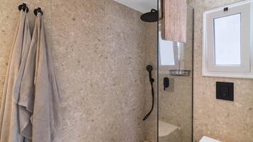 A bathroom with a glass shower enclosure, a towel rack with towels, a toilet, and a window.