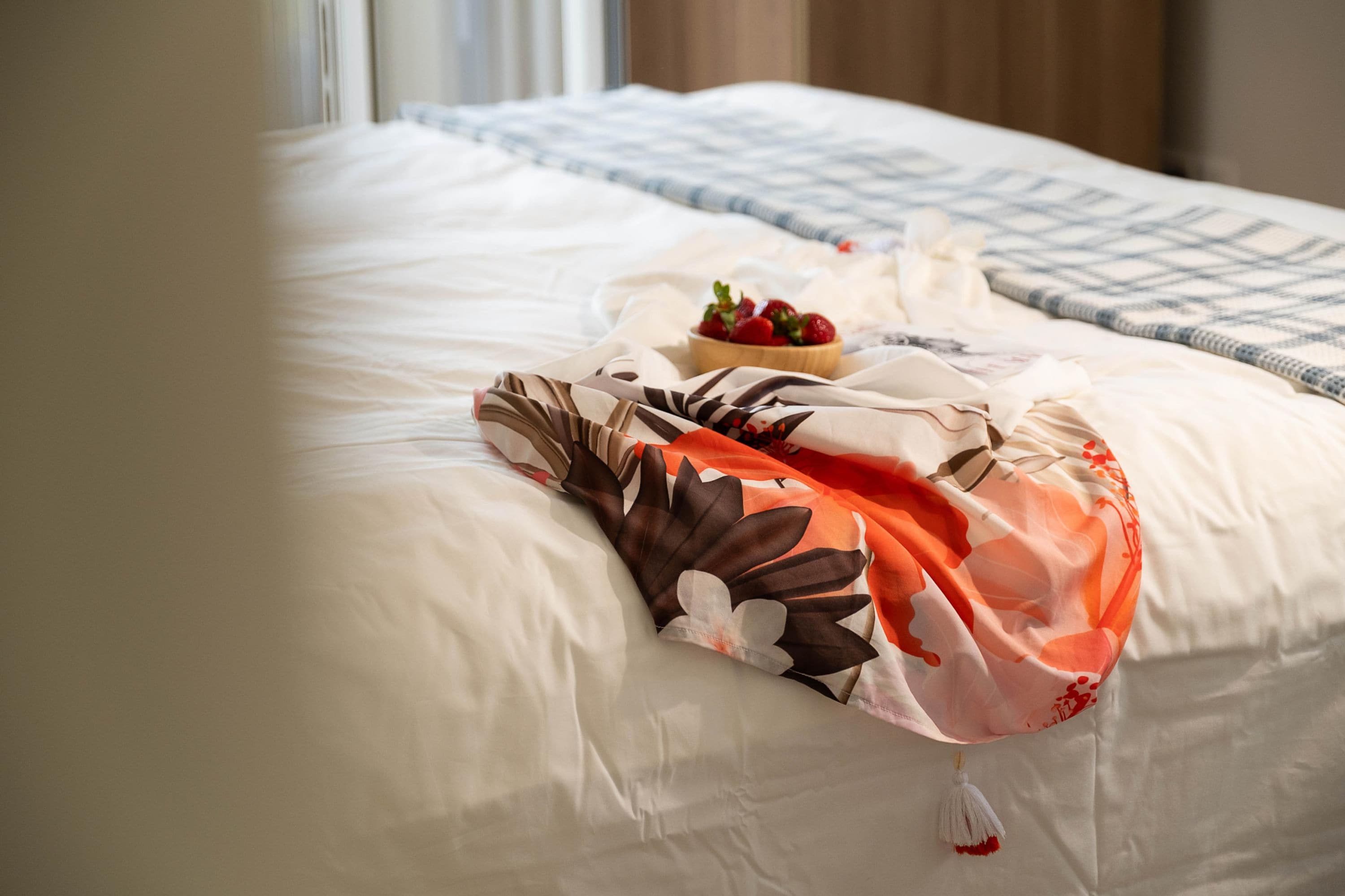 Una cama bien hecha con un edredón estampado con motivos florales, un bol de fresas y una almohada blanca.