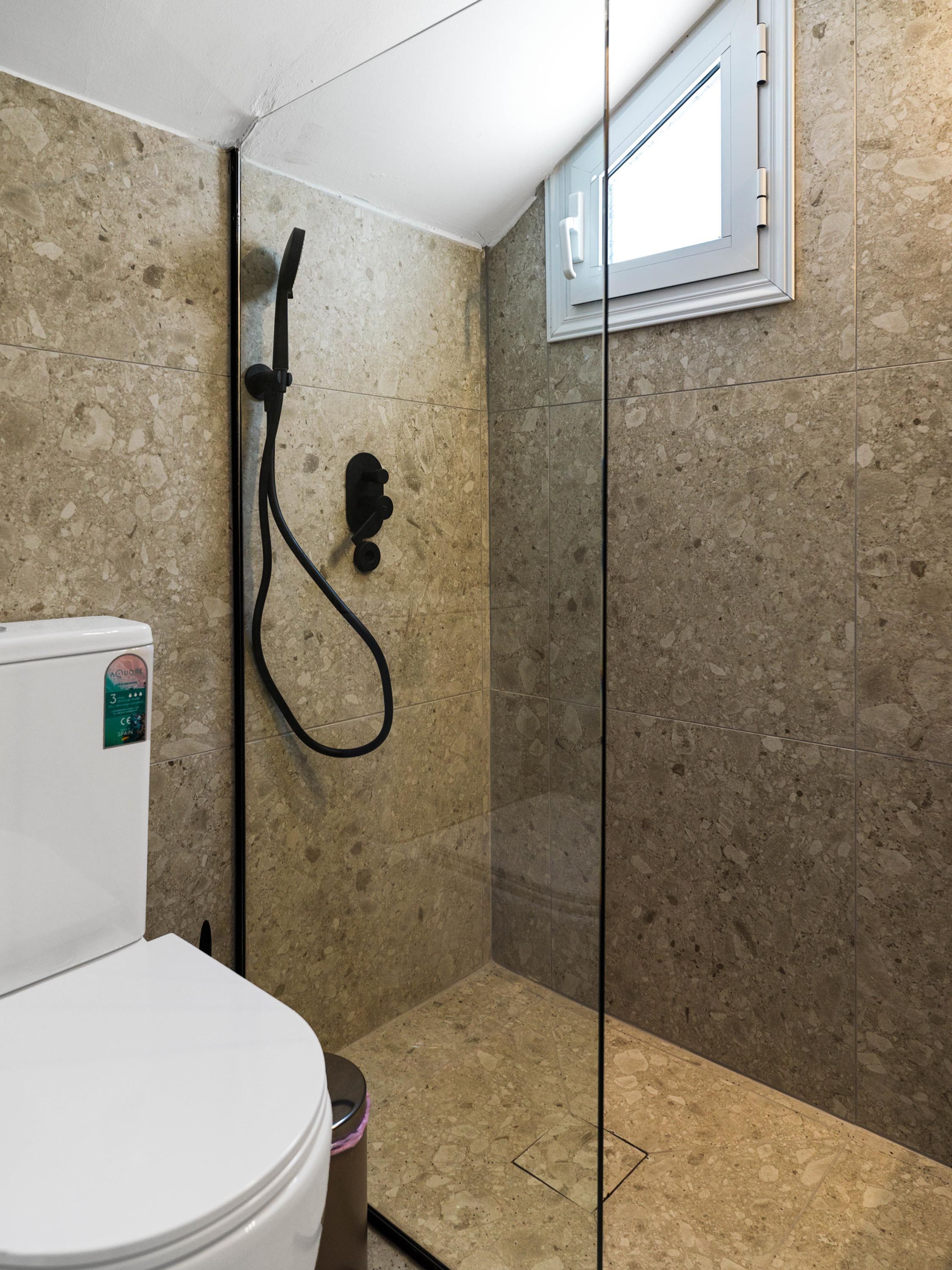 Un baño con inodoro, cabina de ducha y ventana.