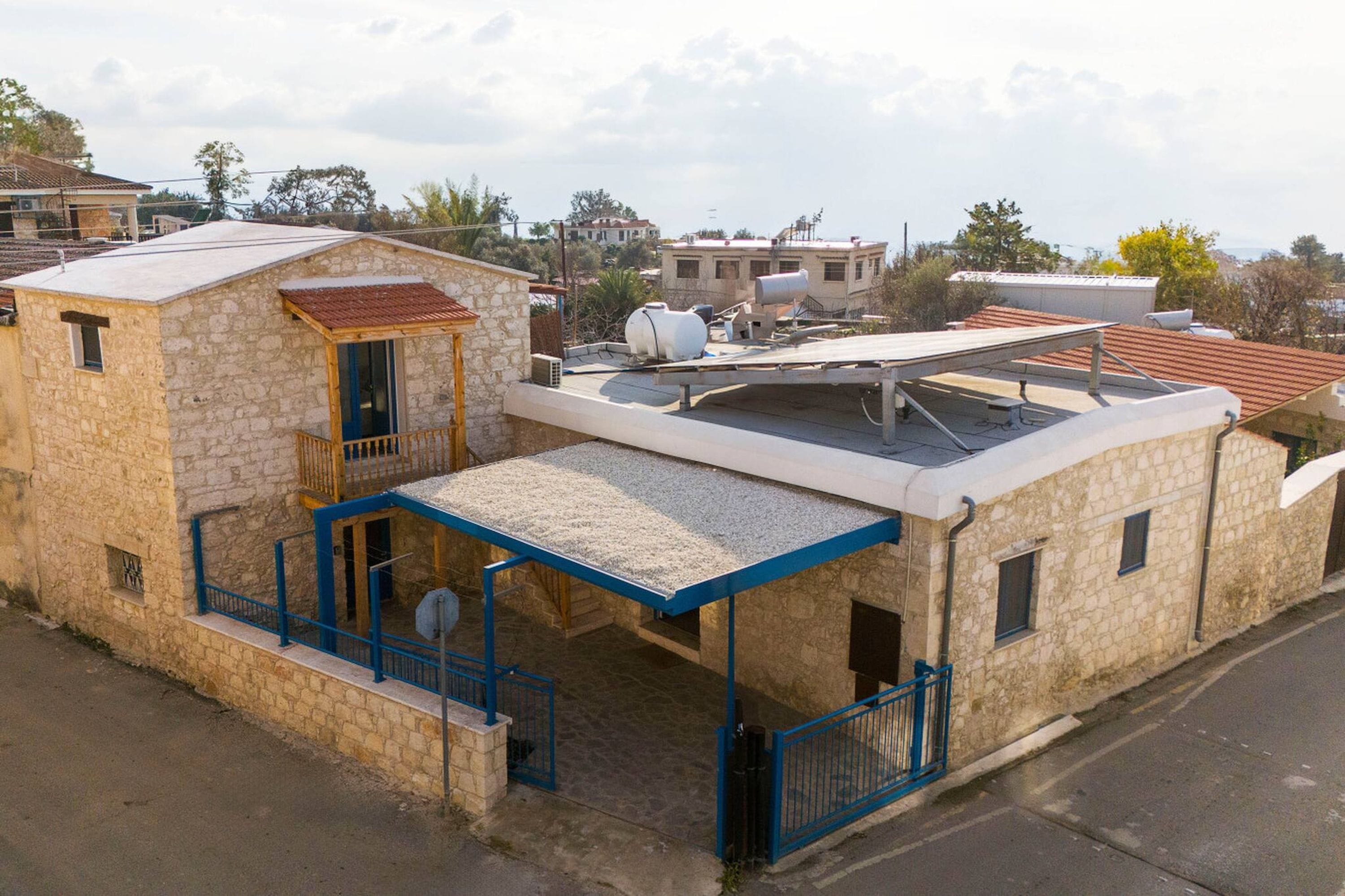Un edificio de piedra con techo plano, un espacio al aire libre cubierto y vistas del barrio circundante.