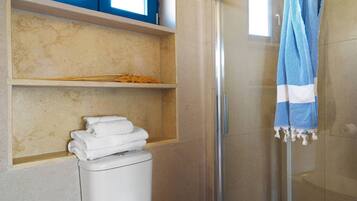 Un baño con cabina de ducha de vidrio, inodoro y toallero con toallas dobladas.