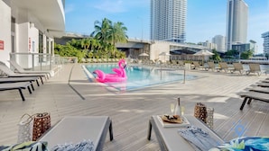 A rooftop pool area with lounge chairs, a pink flamingo float, and high-rise buildings in the background. - Apt With Private Balcony - Incredible Pool (Hallandale Beach)