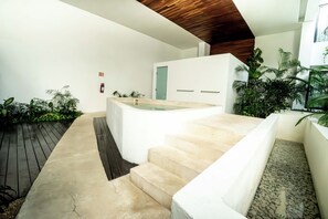 Ein moderner Außenbereich mit Whirlpool und Treppe, umgeben von viel Grün und einer Holzterrasse.