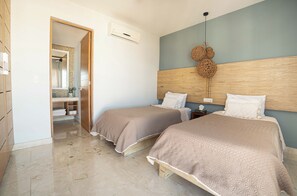 Ein Hotelzimmer mit zwei Betten, einem Holz-Kopfteil, einem Spiegel und einem durch eine offene Tür einsehbaren Badezimmer.