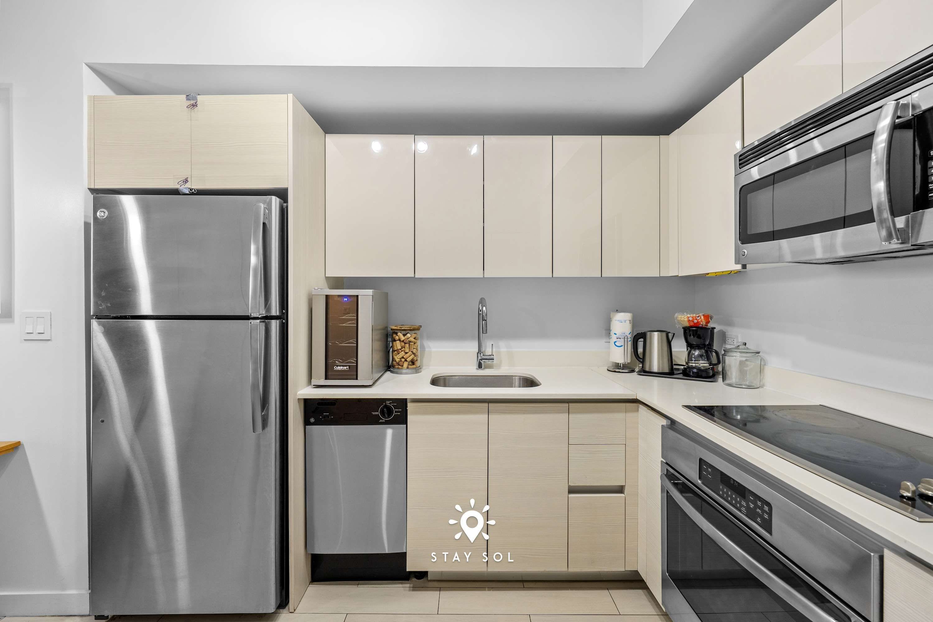 A modern kitchen with stainless steel appliances, light wood cabinets, and a built-in dishwasher.
