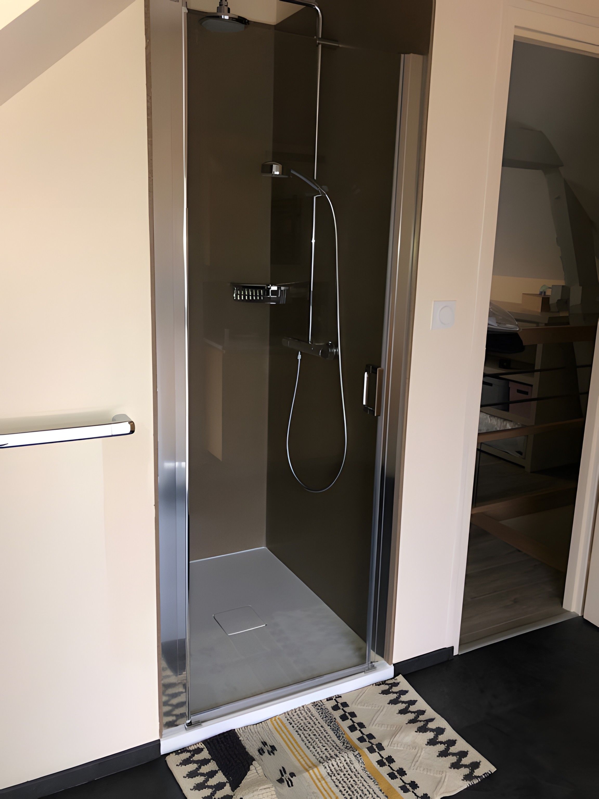 A glass-enclosed shower with a handheld showerhead and a handheld faucet.