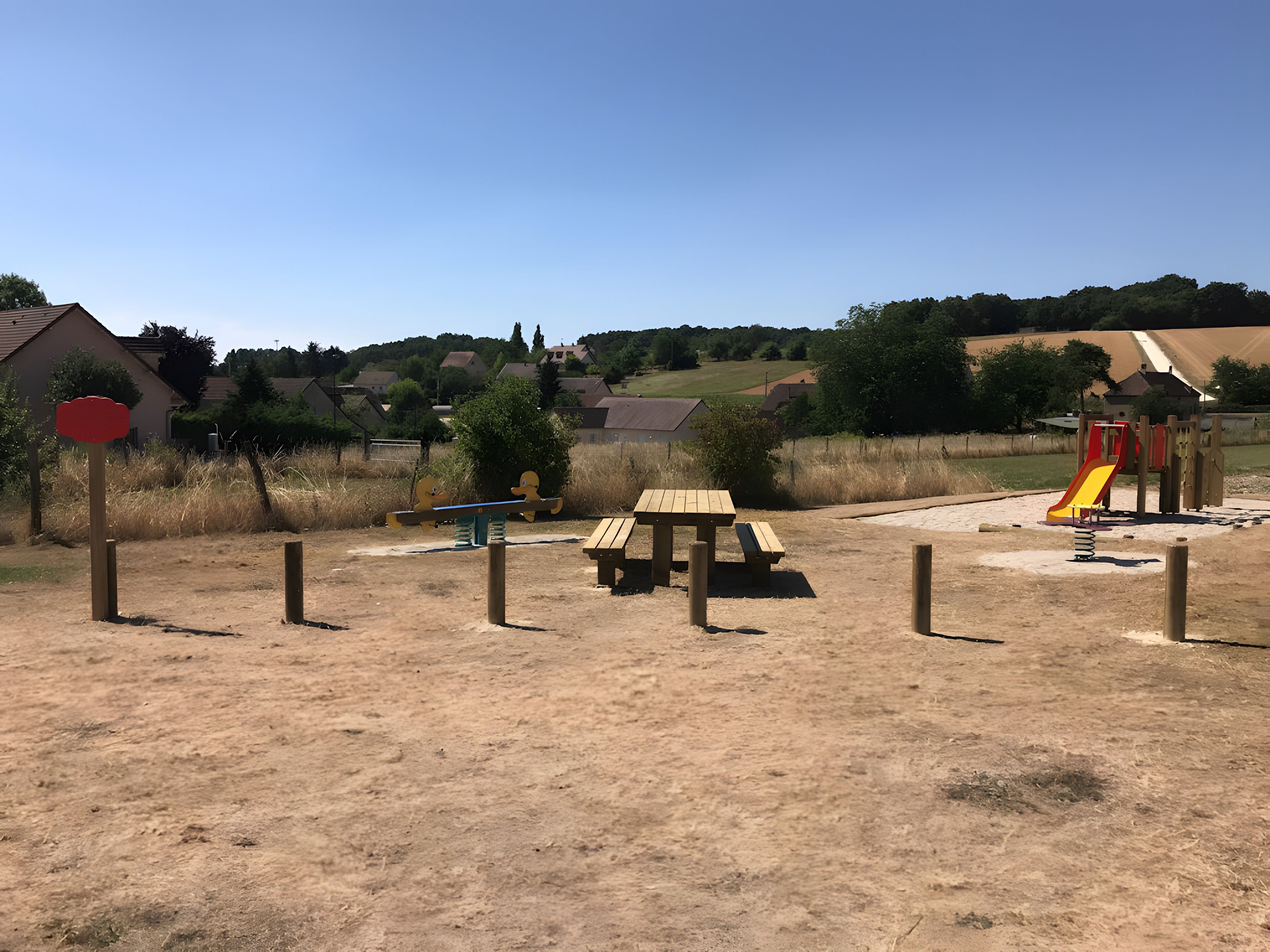 A playground with a slide and swings, surrounded by a fence and open space.