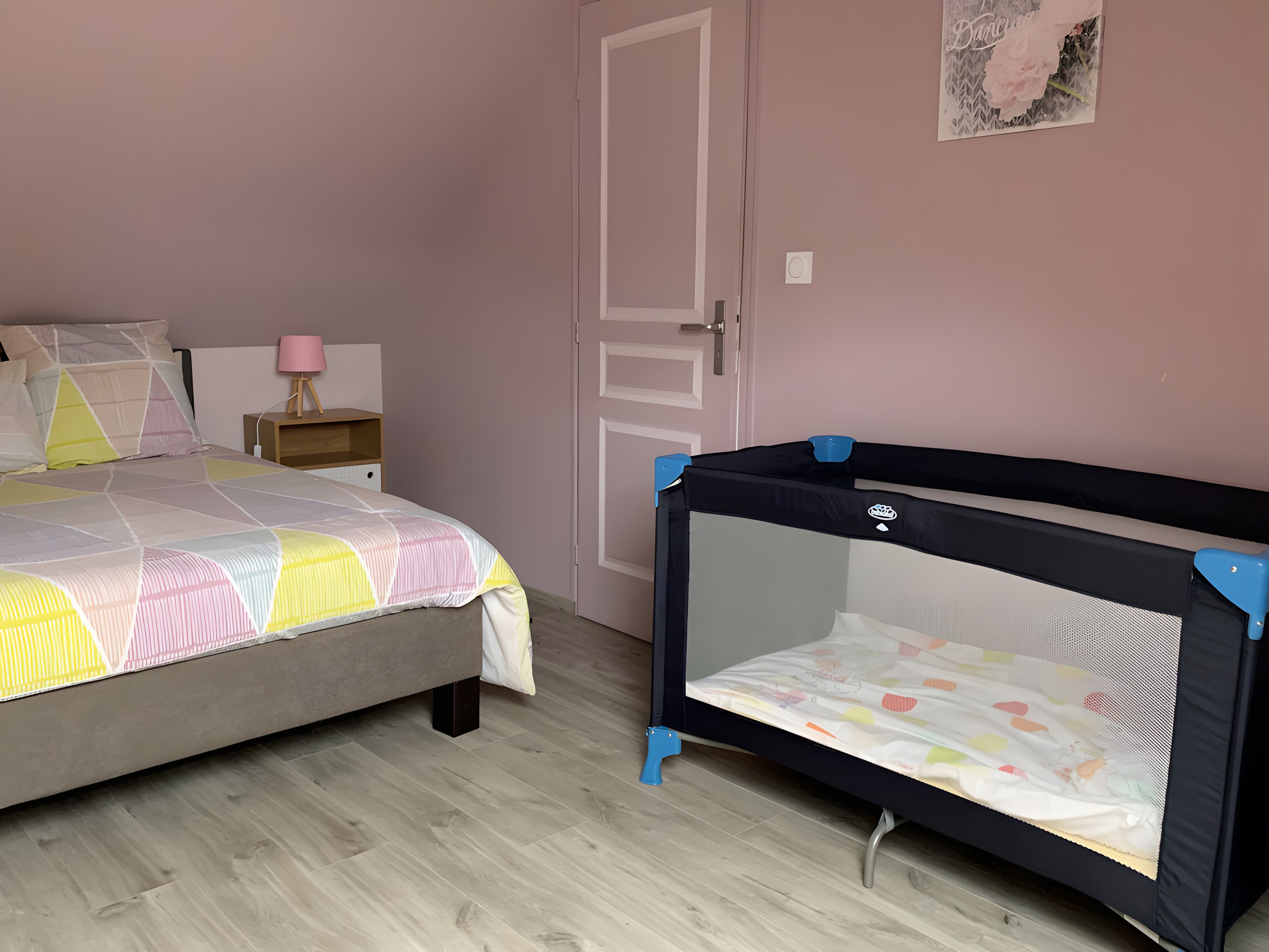 Une chambre à coucher avec un lit, une table de chevet, une porte et un parc pour bébé.