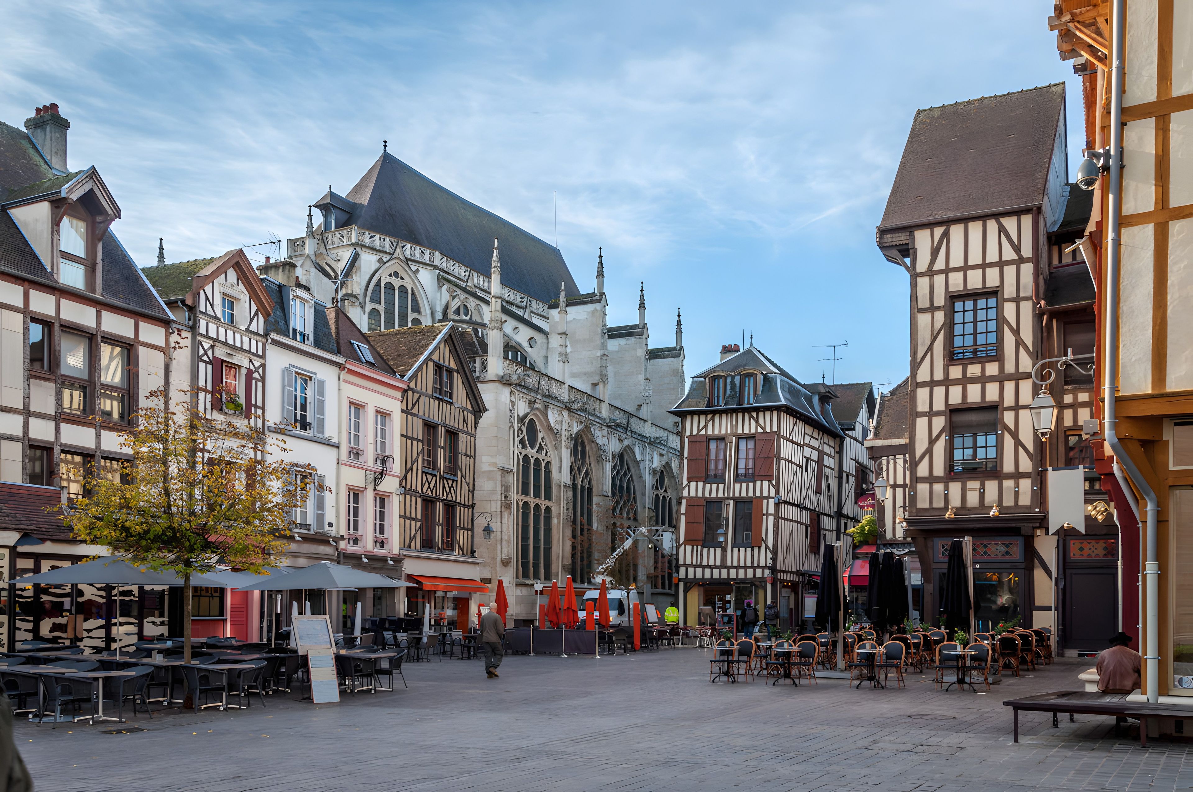 A historic European town square with traditional half-timbered buildings, outdoor seating areas, and a prominent church with a large dome.