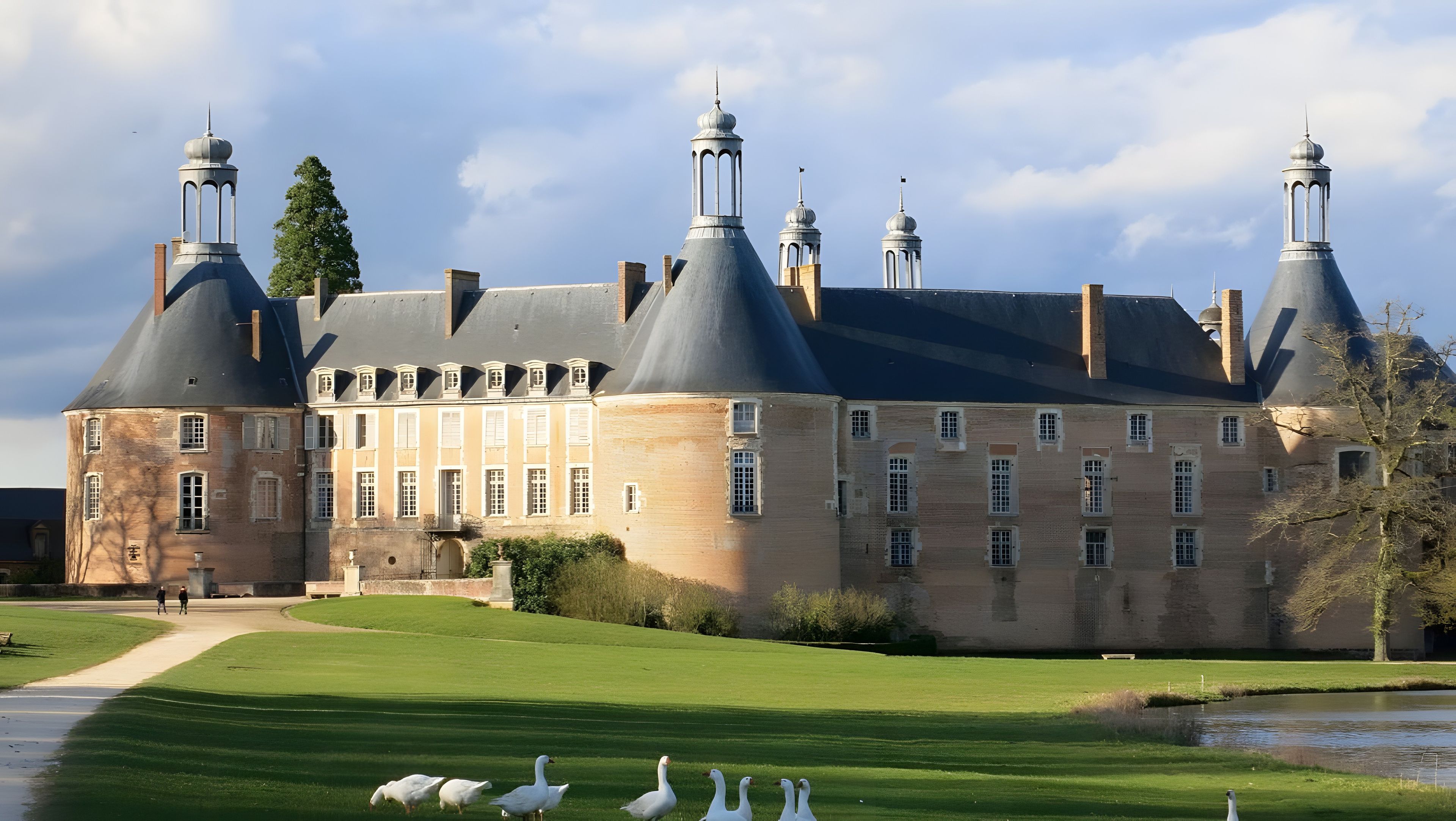 A large historic building with multiple towers and a well-maintained lawn.