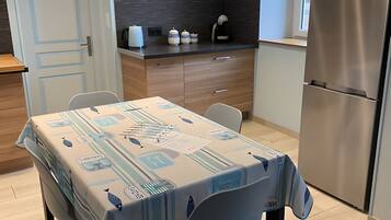 Moderni keittiö, jossa on ruokapöytä, tuoleja, kello ja jääkaappi.