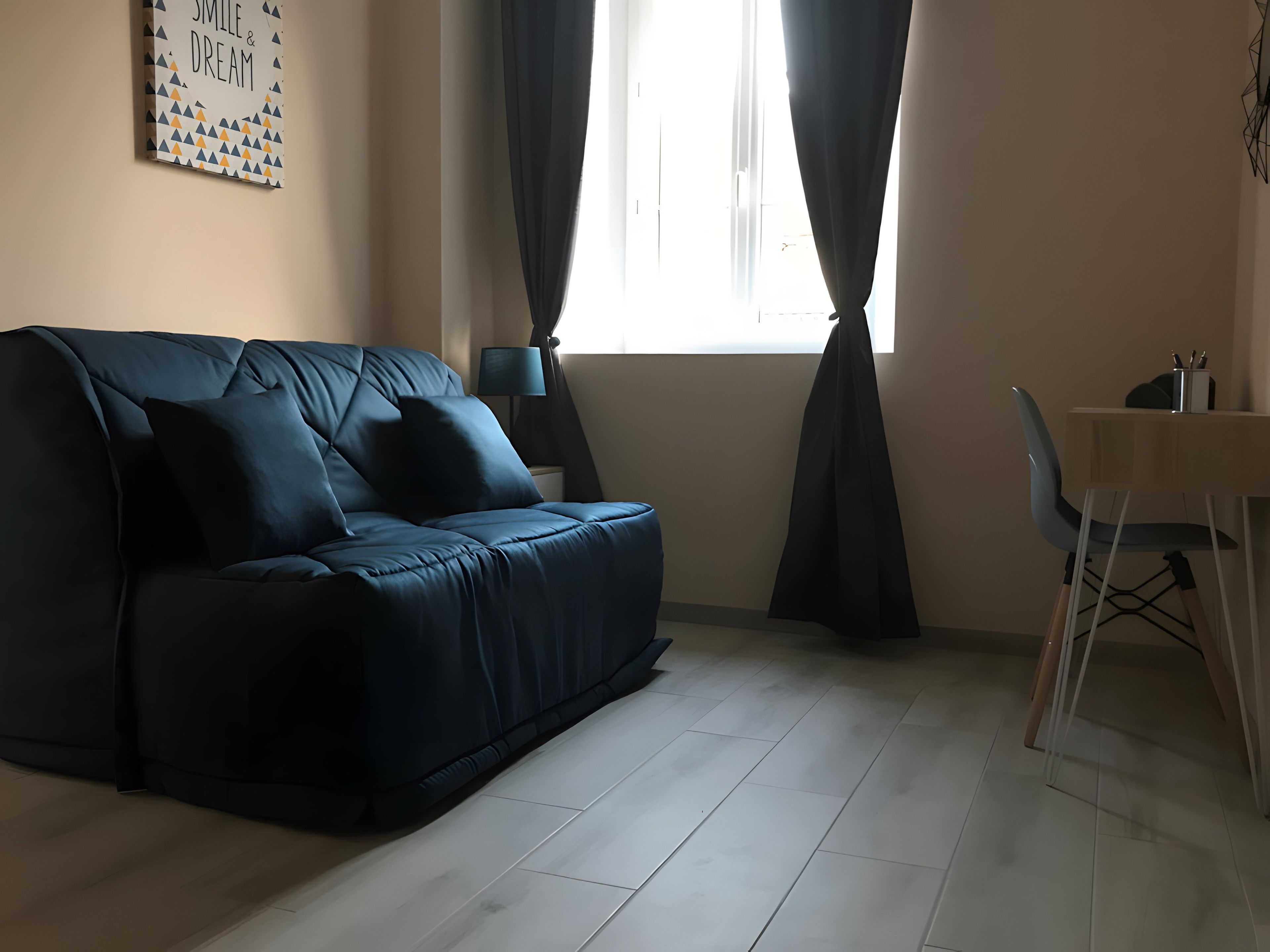 Una sala de estar moderna con un sofá azul oscuro, una mesita con una lámpara y una ventana con cortinas.