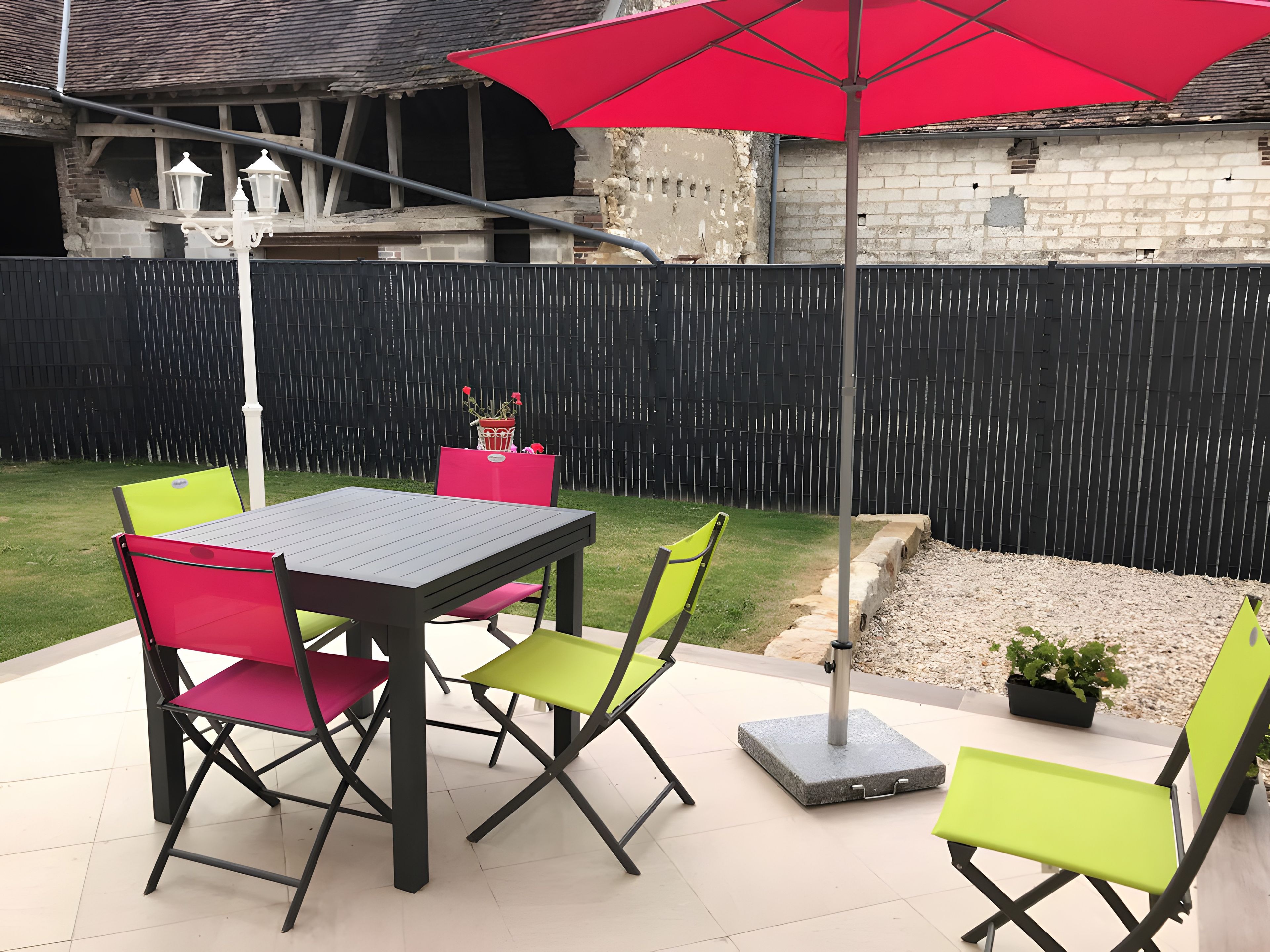 An outdoor patio with a table and chairs, a red umbrella, and a black fence.