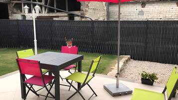 An outdoor patio with a table and chairs, a red umbrella, and a black fence.