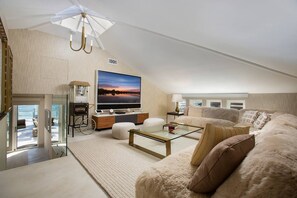 Uma sala de estar moderna com uma grande televisão de tela plana, uma máquina de pipoca e uma área de estar aconchegante, com um sofá e um banquinho.