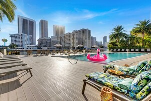 A rooftop pool area with lounge chairs, a pink flamingo float, and a city skyline in the background.