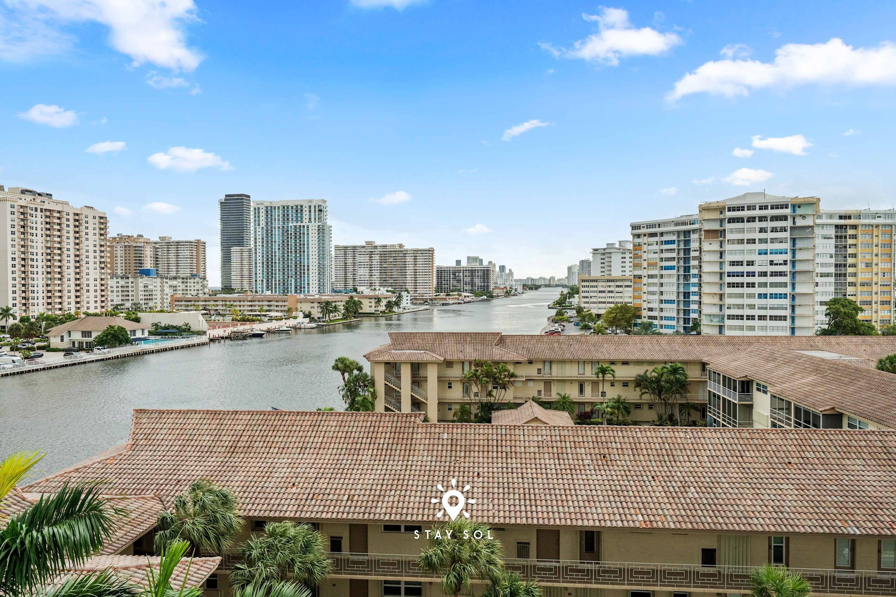 A riverside view of a city with high-rise buildings and a hotel with a tiled roof.