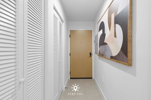 A hallway with a door at the end, a wall-mounted artwork, and a light fixture on the ceiling. - Sophisticated Studio w Pools (Miami)