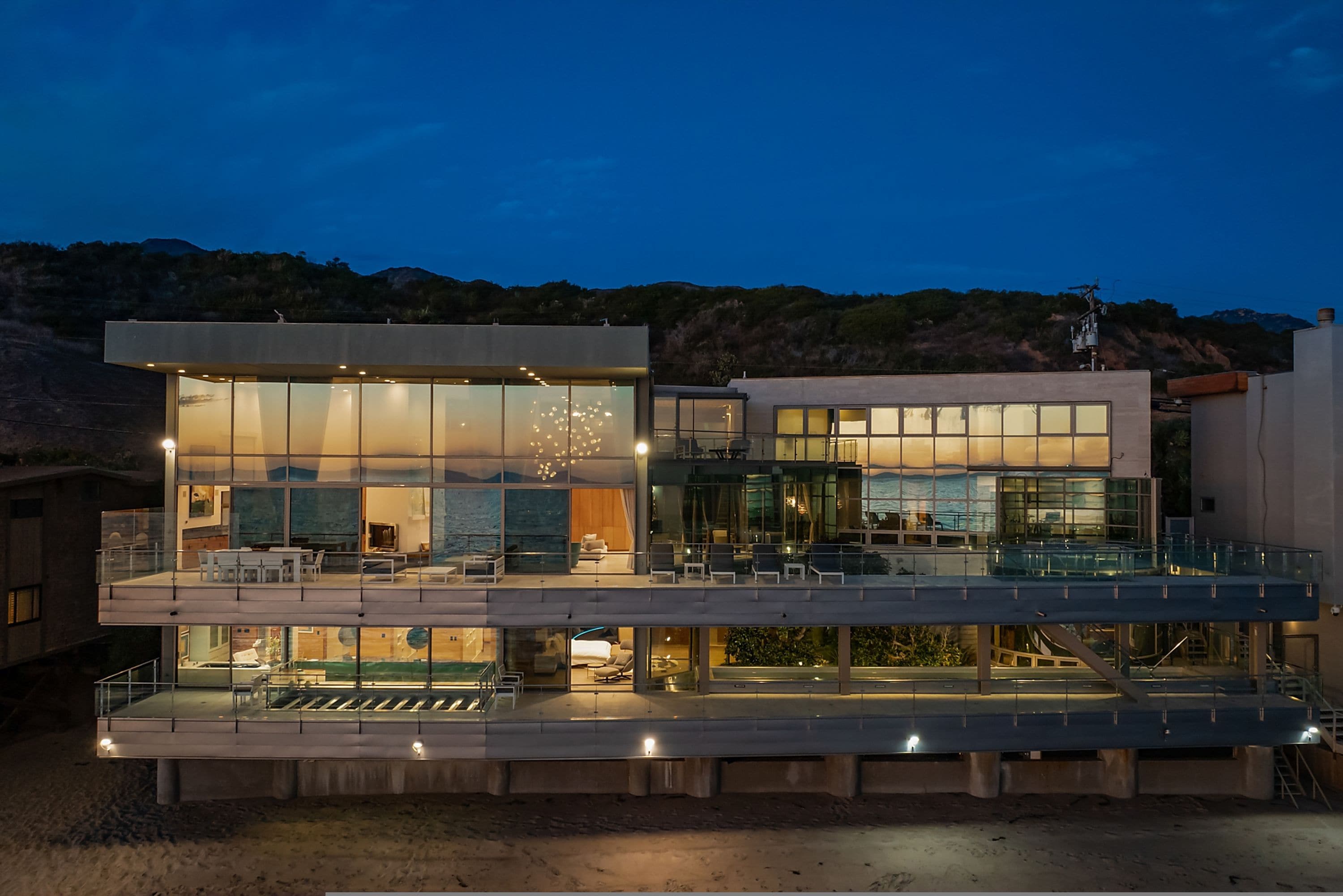 A modern two-story house with large glass windows, a balcony, and a pool area.