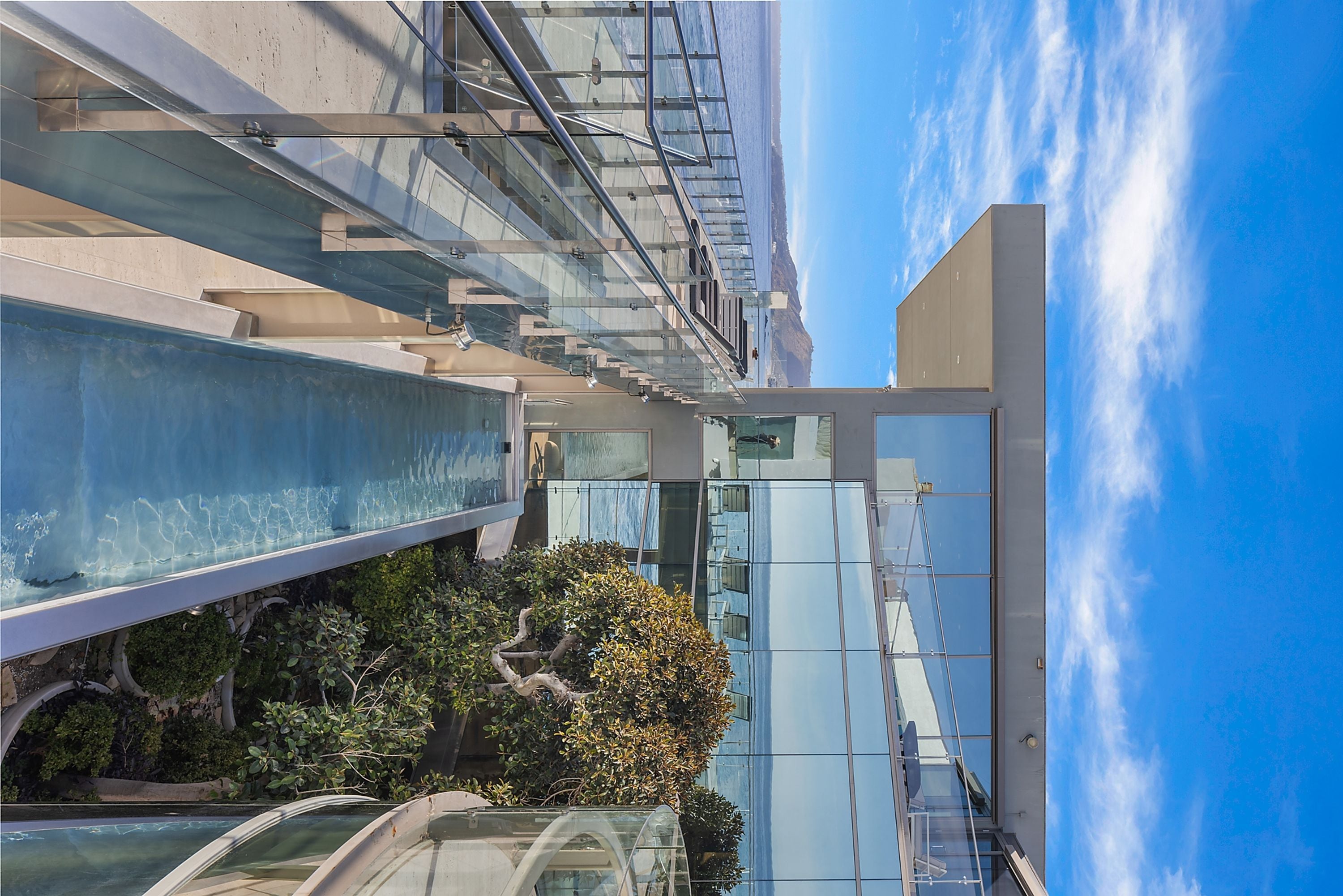 Um edifício moderno com fachada de vidro, piscina e céu claro.