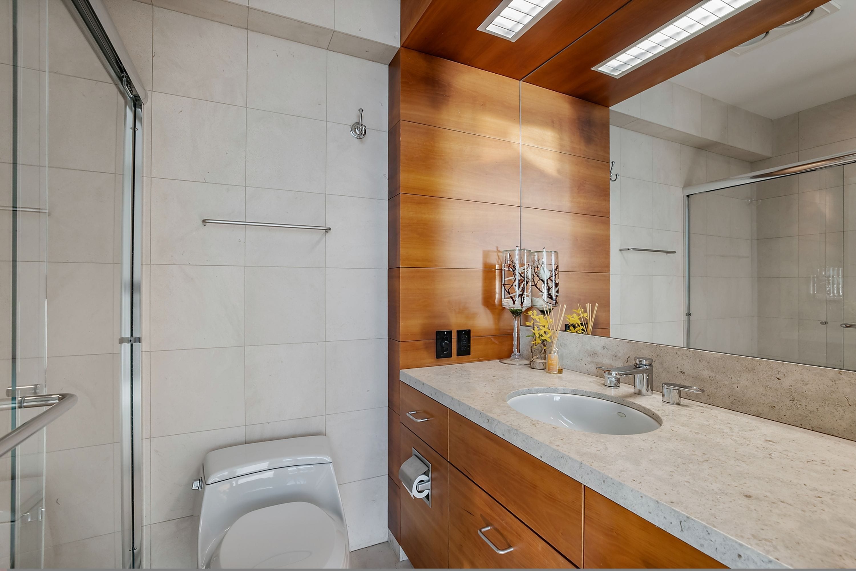 A modern bathroom with a large mirror, two sinks, and a toilet.
