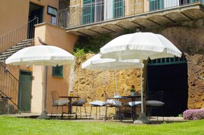 A terrace with outdoor seating, white umbrellas, and a stone wall backdrop.