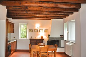 A kitchen with wooden cabinets, a dining table with chairs, a fireplace, and a window with curtains. - Montecasciano Oleandro (Capranica)