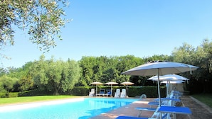 Una piscina con lettini e ombrelloni, immersa nel verde.