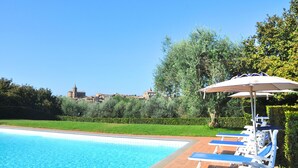 Una piscina con lettini e un ombrellone, immersa nel verde e con vista su un edificio storico.