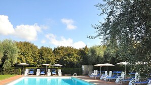 Una piscina con lettini e ombrelloni, immersa nel verde.