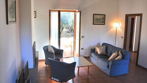 A living room with a sofa, a chair, a table, and a lamp. There is a door leading to an outdoor area. - Montecasciano Mimosa (Capranica)