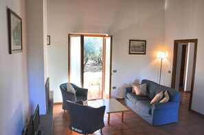A living room with a sofa, a chair, a table, and a lamp. There is a door leading to an outdoor area. - Montecasciano Mimosa (Capranica)