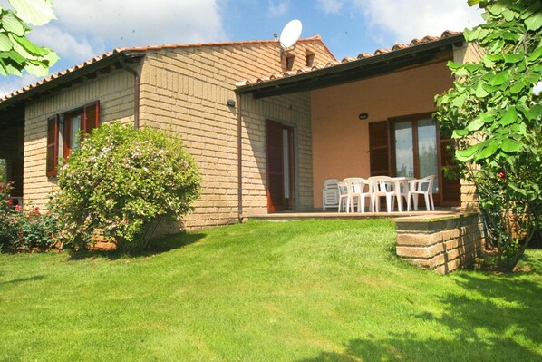A two-story house with a brick exterior, a satellite dish, and a small patio with plastic chairs.