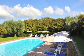 A swimming pool with lounge chairs and umbrellas, surrounded by a hedge and trees.