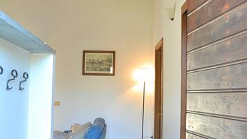 A hallway with a wooden door, a blue sofa, a floor lamp, and a framed picture on the wall.