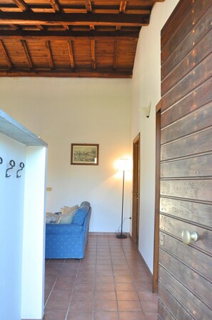 A hallway with a wooden door, a blue sofa, a floor lamp, and a framed picture on the wall.