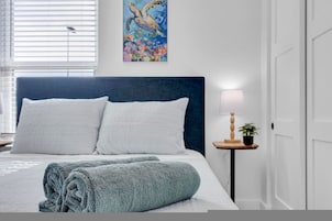 Una cama bien hecha con ropa de cama blanca y azul, un cabecero azul y un cuadro de una tortuga marina en la pared.