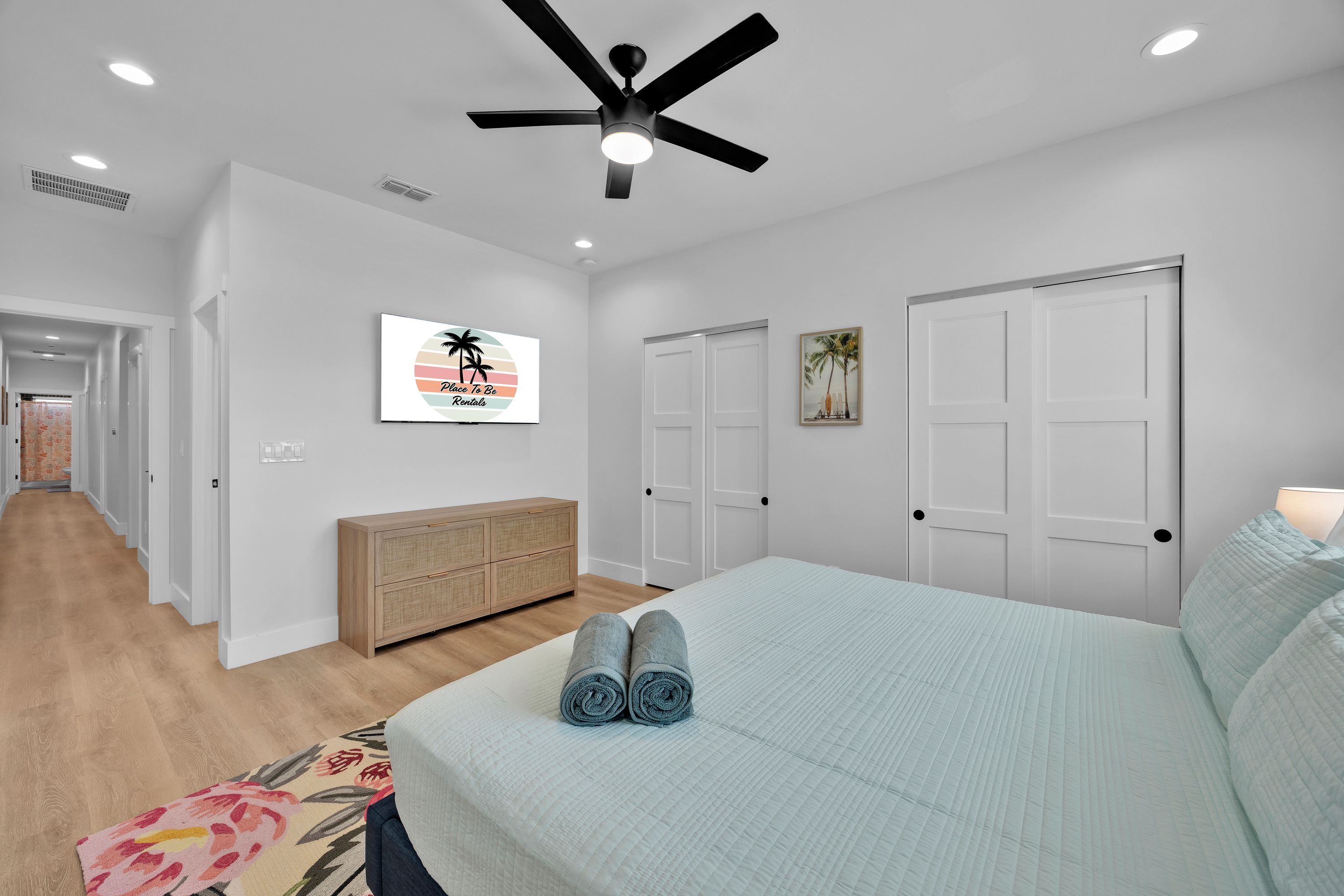 A bedroom with a bed, a ceiling fan, a dresser, and a door.