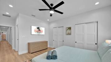 A bedroom with a bed, a ceiling fan, a dresser, and a door.