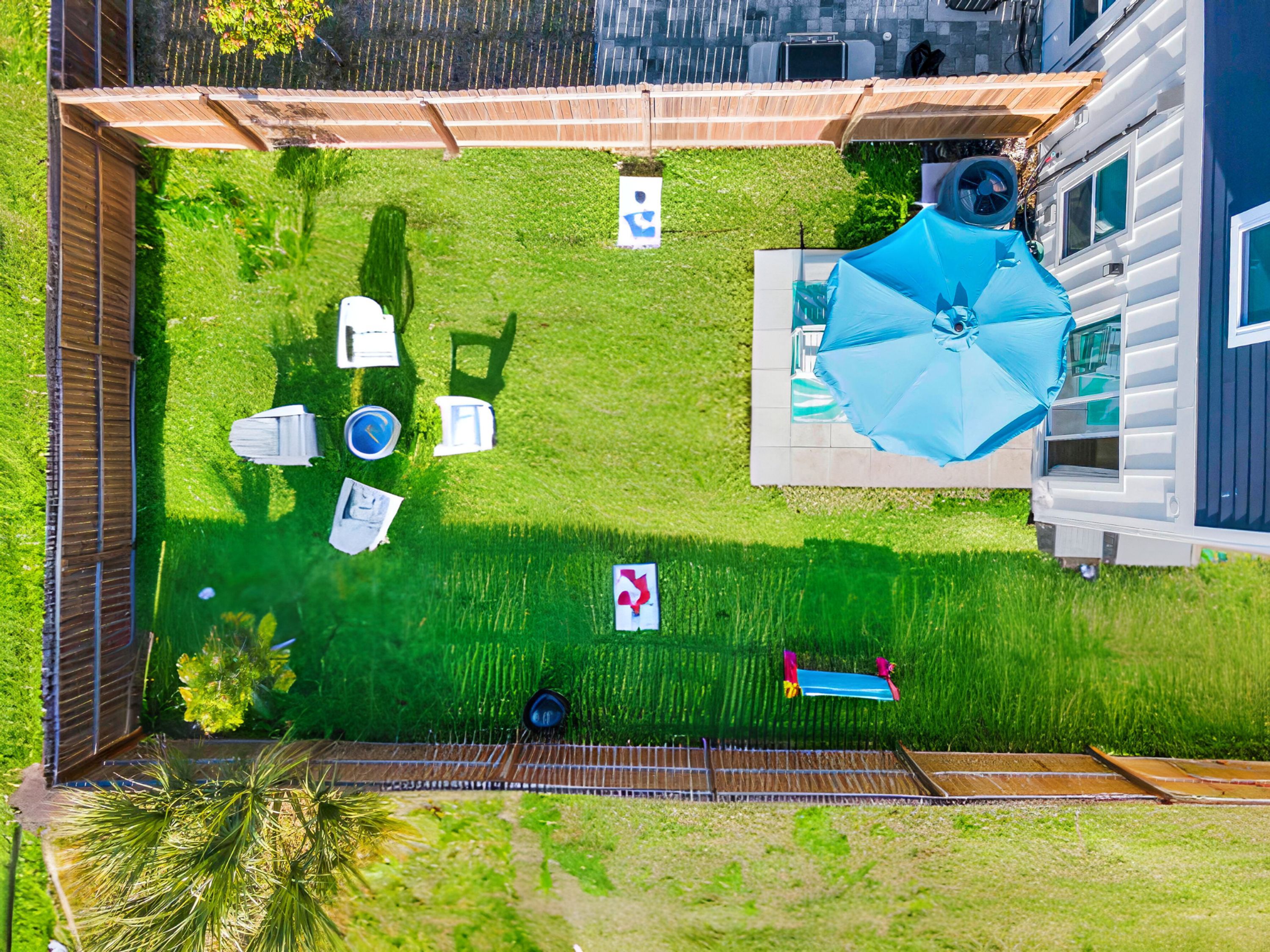 An aerial view of a backyard with a lawn, patio furniture, a pool, and a house.
