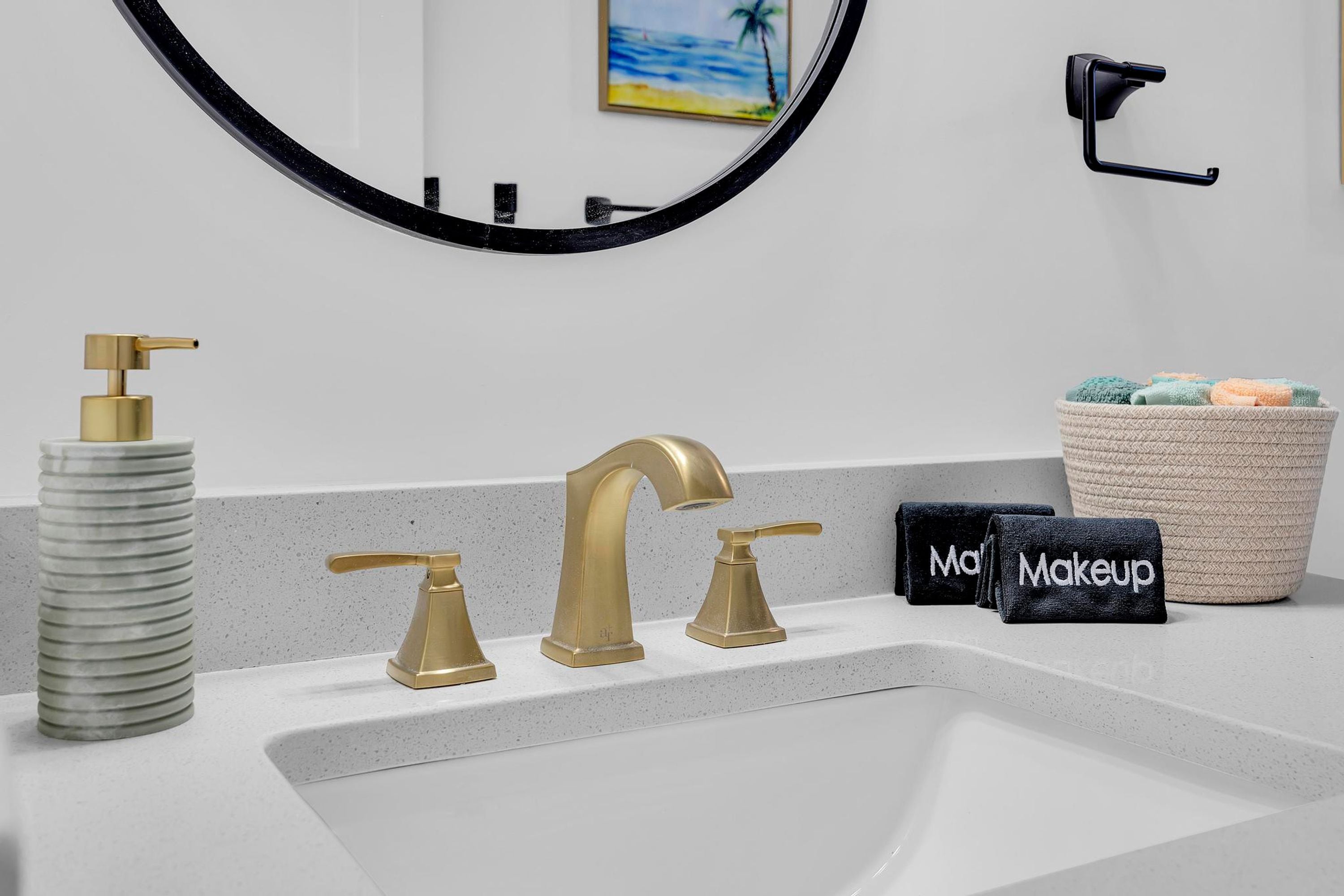 A bathroom with a white sink, gold faucets, a soap dispenser, and a towel rack.