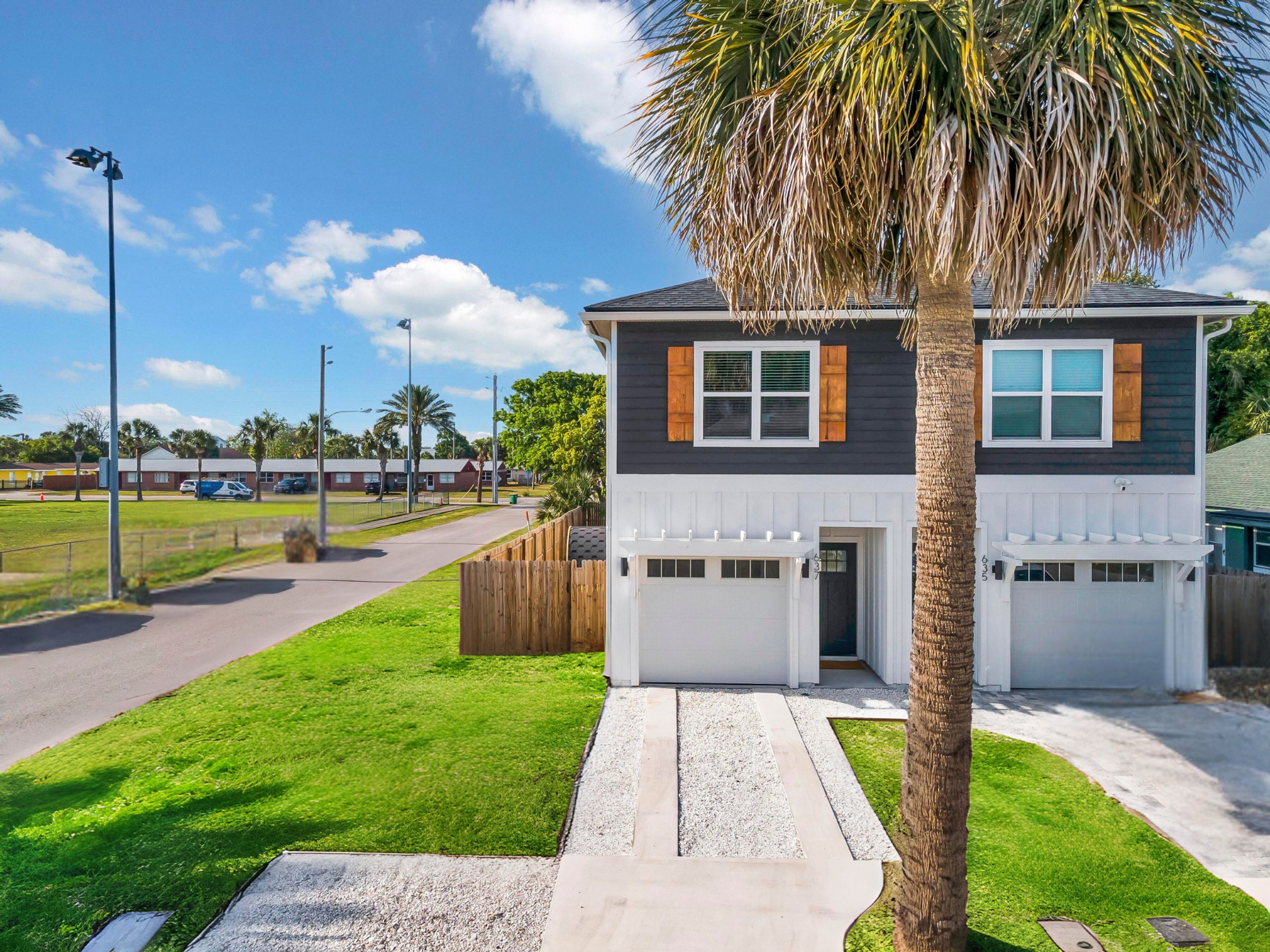 A two-story house with a garage, a well-maintained lawn, and a palm tree.