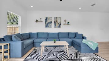 Un soggiorno moderno con un divano ad angolo blu, un tavolino in legno e un tappeto dal motivo geometrico.