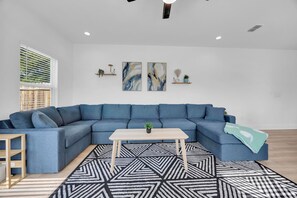 Una sala de estar moderna con un sofá seccional azul, una mesa de centro de madera y una alfombra con diseño geométrico.