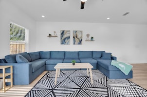 A modern living room with a blue sectional sofa, a wooden coffee table, and a geometric patterned rug.