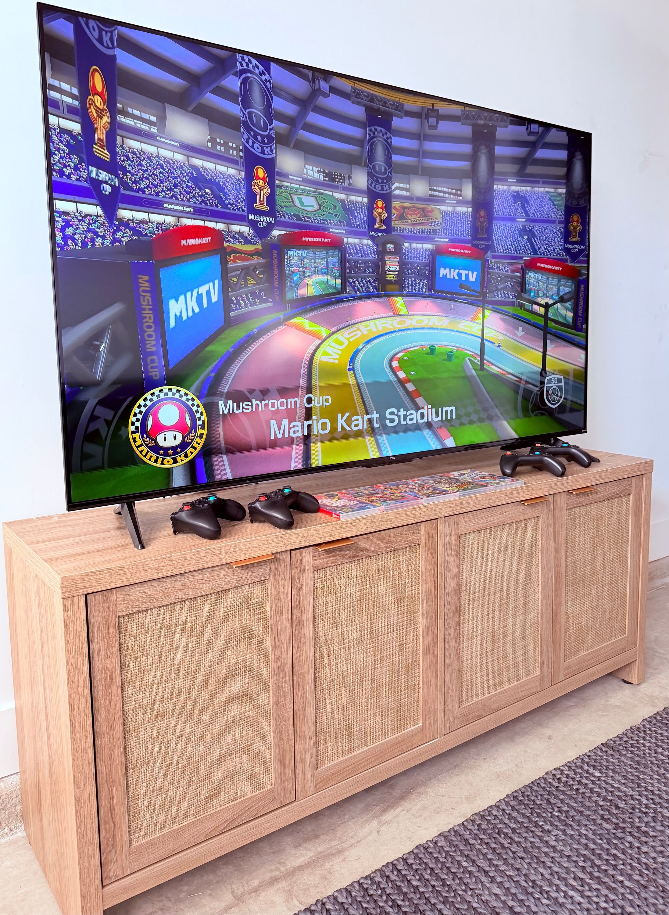 A television displaying a Mario Kart game, mounted on a wooden cabinet with a woven front panel.