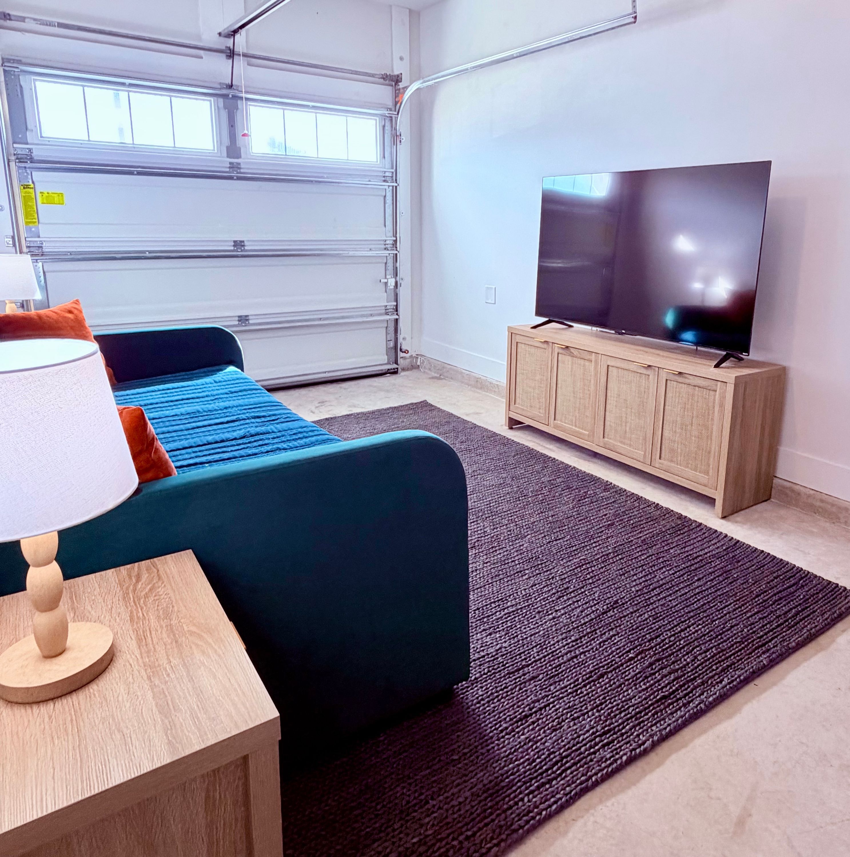 A room with a bed, a television on a wooden cabinet, a lamp, and a garage door.